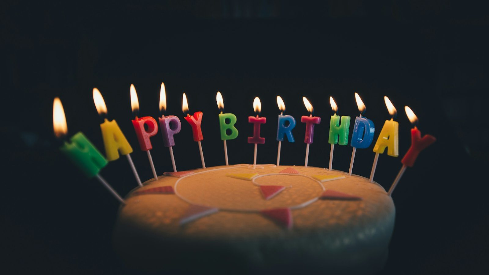 Birthday cake with lit Happy Birthday letter candles