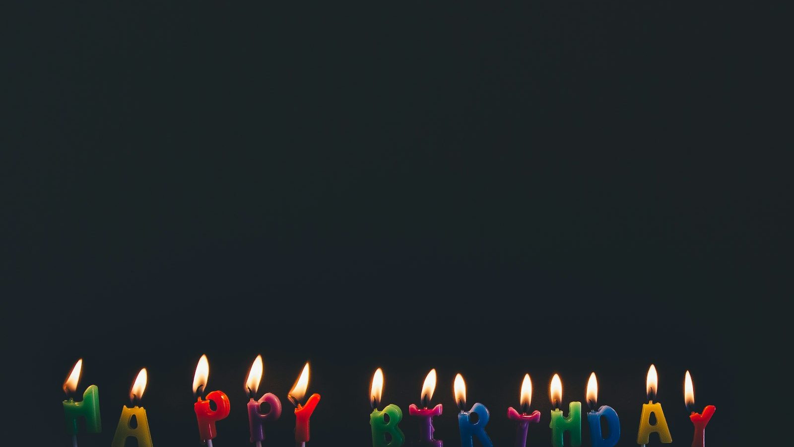 Row of lit Happy Birthday candles in assorted colours