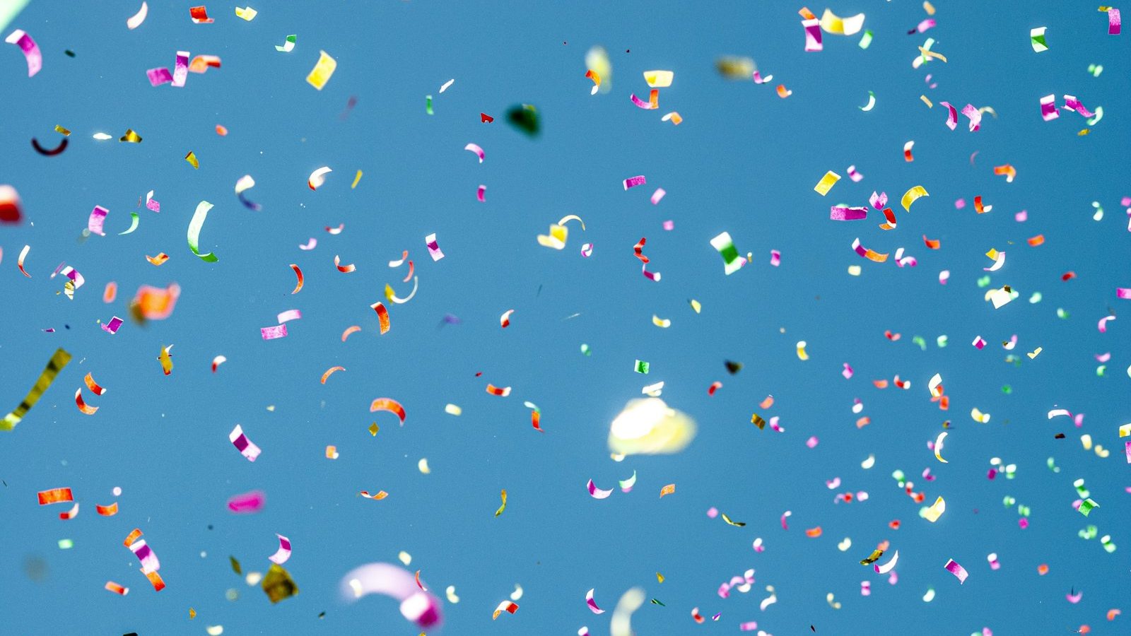 Colourful confetti falling against a blue sky